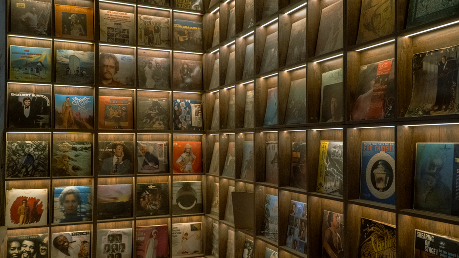 A wall of neatly arranged vintage vinyl records displayed on lit wooden shelves.